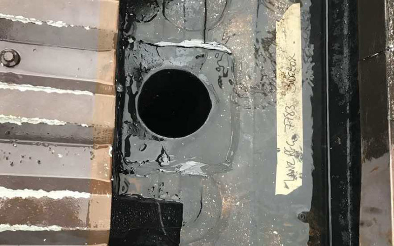 Close-up view of a circular drain hole in a metal surface with water pooling around it and a label visible nearby indicating features of the drainage system optimized for four different functions
